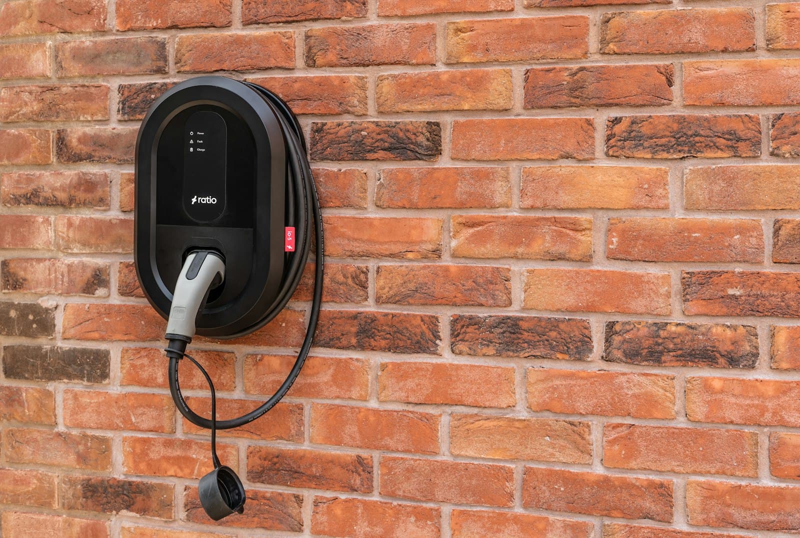 A black wallbox with its charging cable coiled on the unit, mounted on a brick wall.