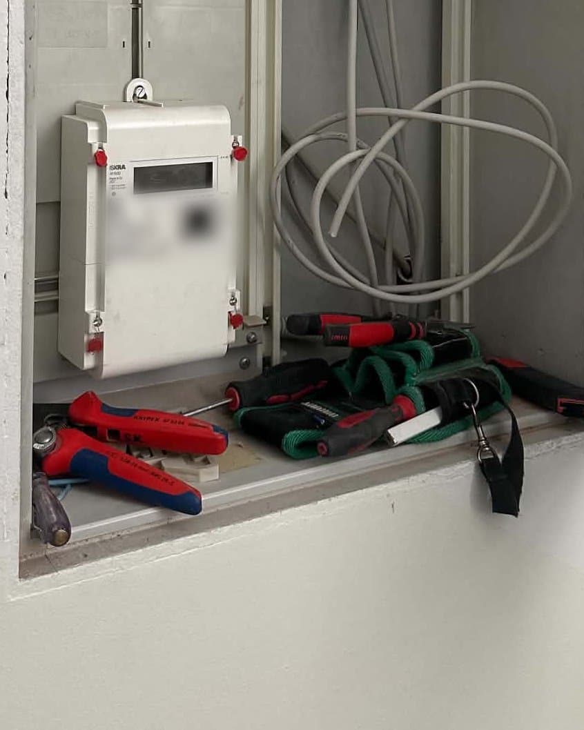 Stromzähler in einem offenen Wandverteiler, davor Zangen, Schraubendreher und eine Werkzeugtasche.